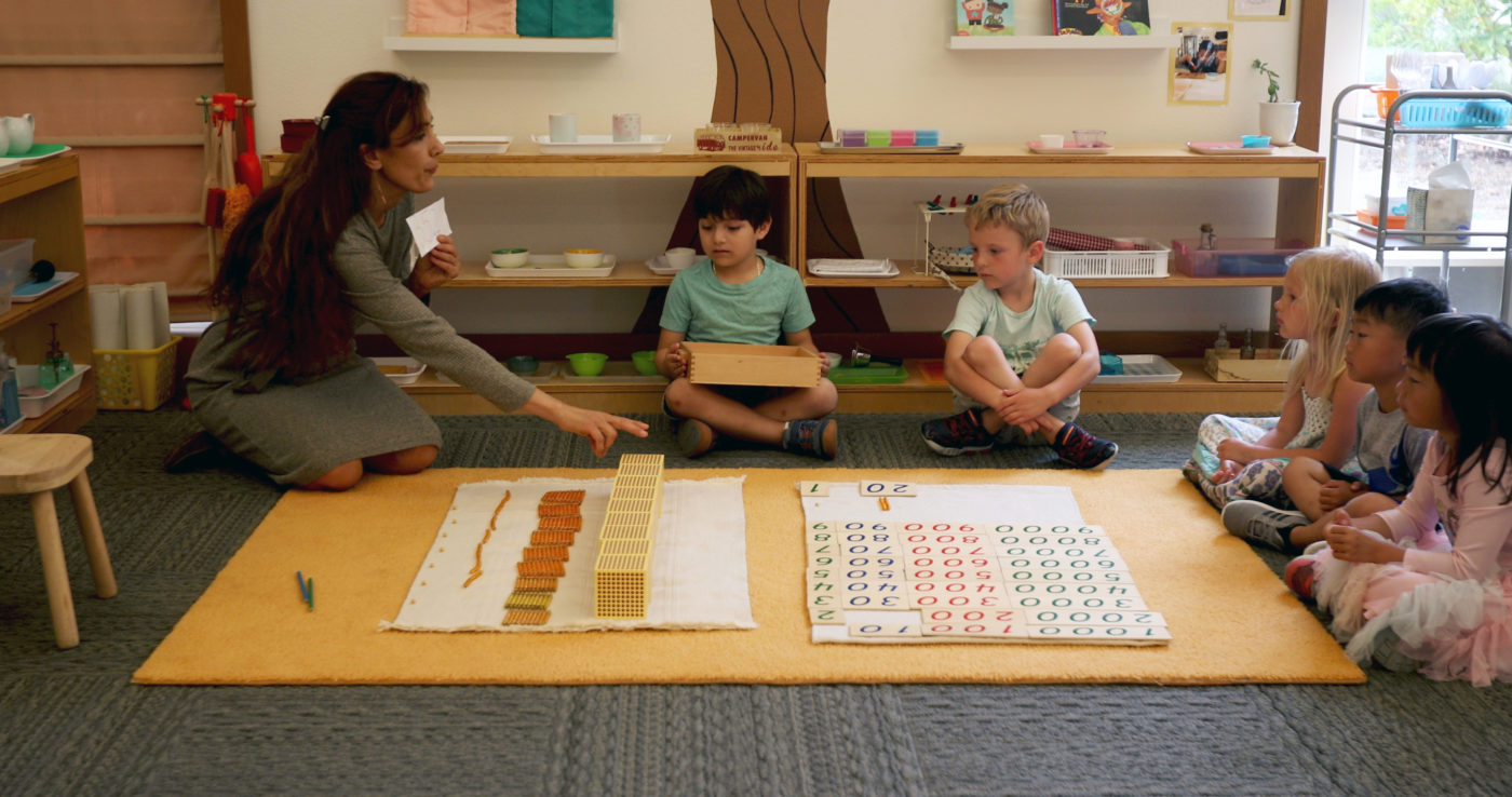 Teacher observing students as they explore Montessori activities independently.